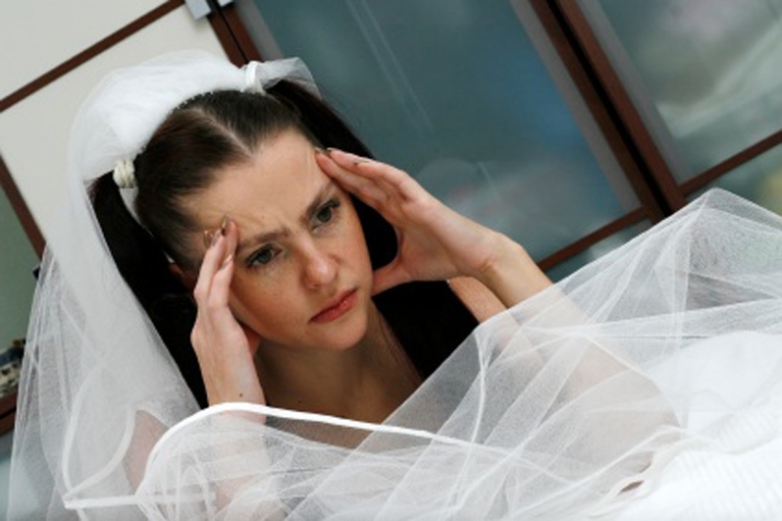 The headache is represented on the face of the beautiful bride in a wedding dress near a bed
